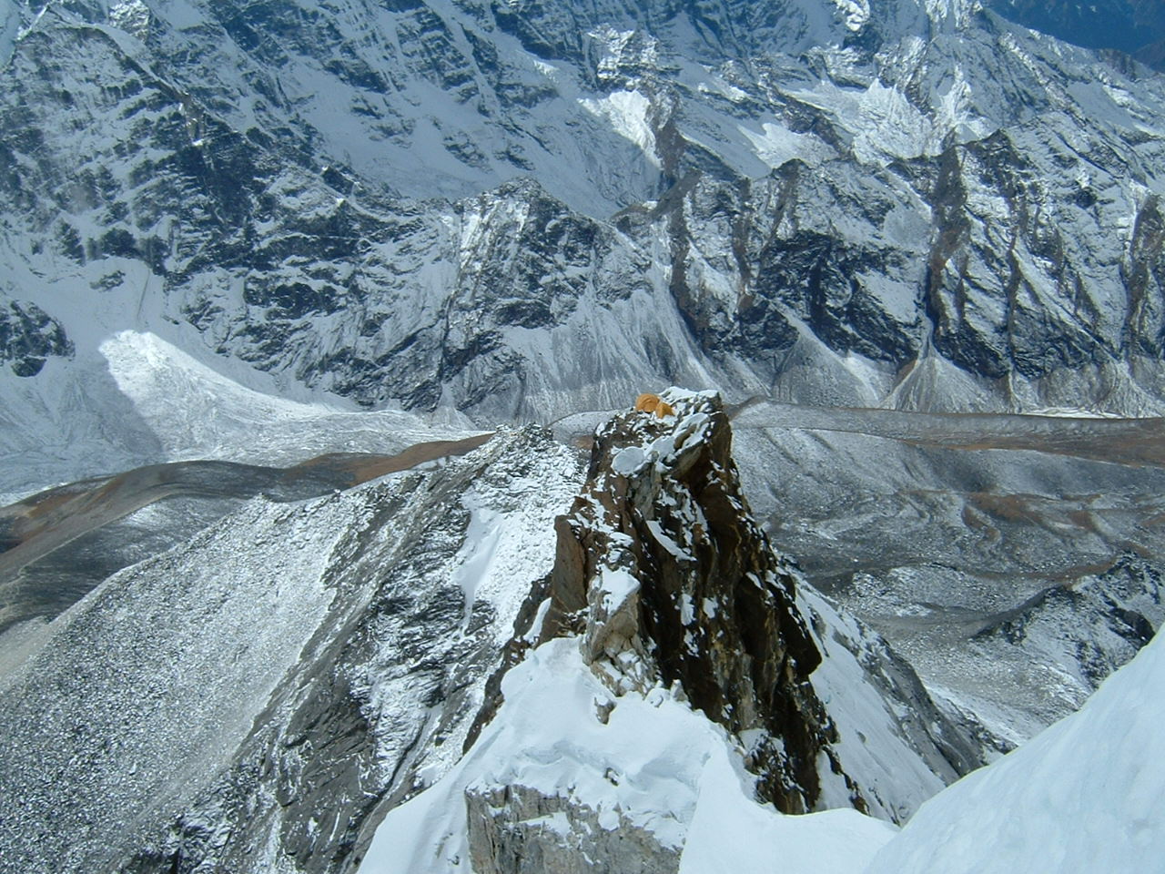 snowy peaks of the Himalayas with two tiny orange tents on a rocky peak