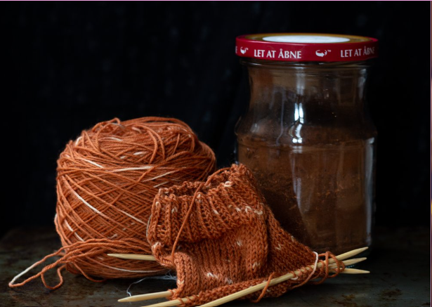 small knitting needles and piece of knitting nest to jar of dyed yarn