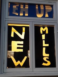 words lit in window saying Eh Up New Mills